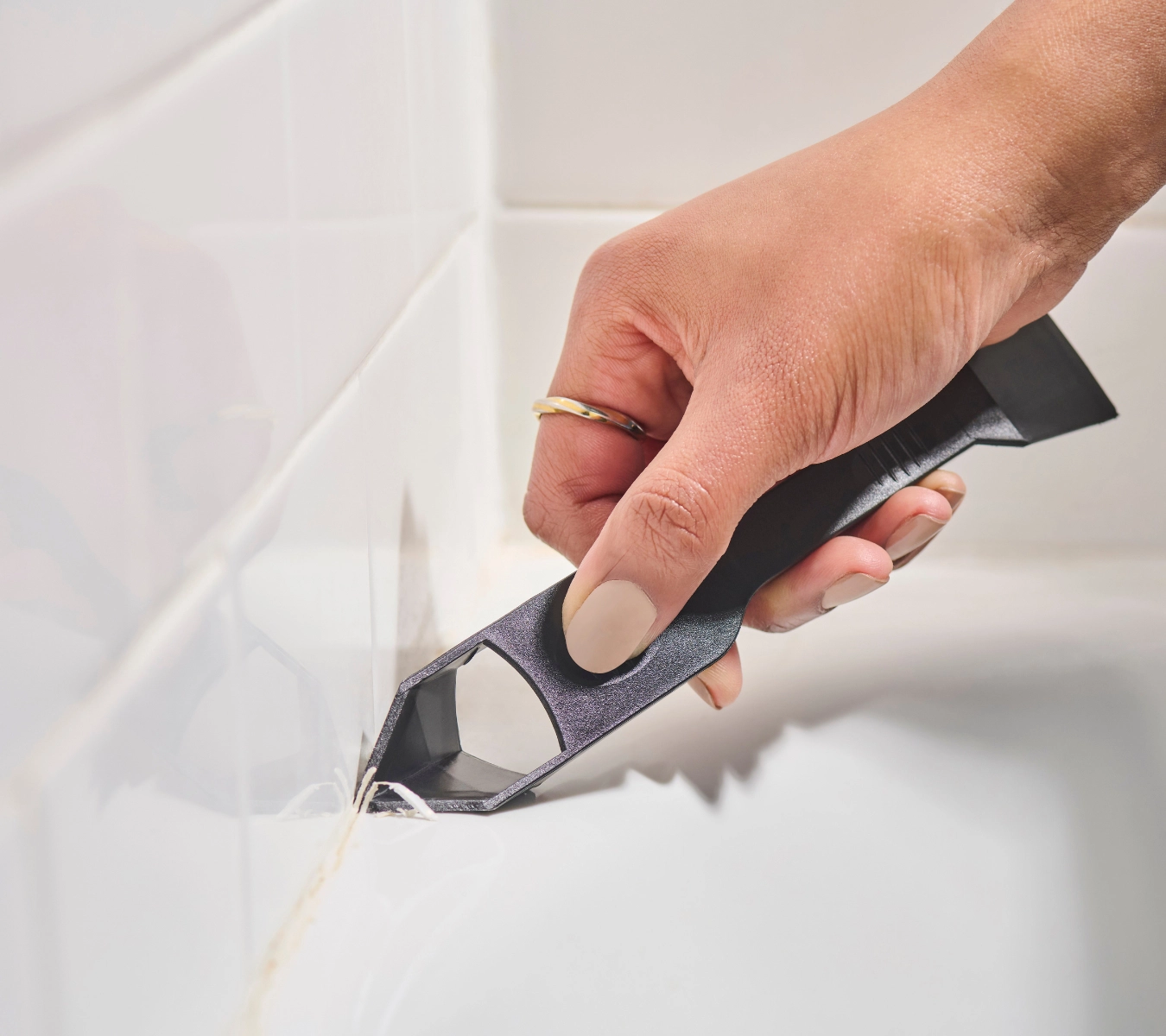 2-a-person-using-the-ge-sealant-remover-tool-to-peel-away-a-line-of-old-sealant-from-a-bathroom-corner-joint